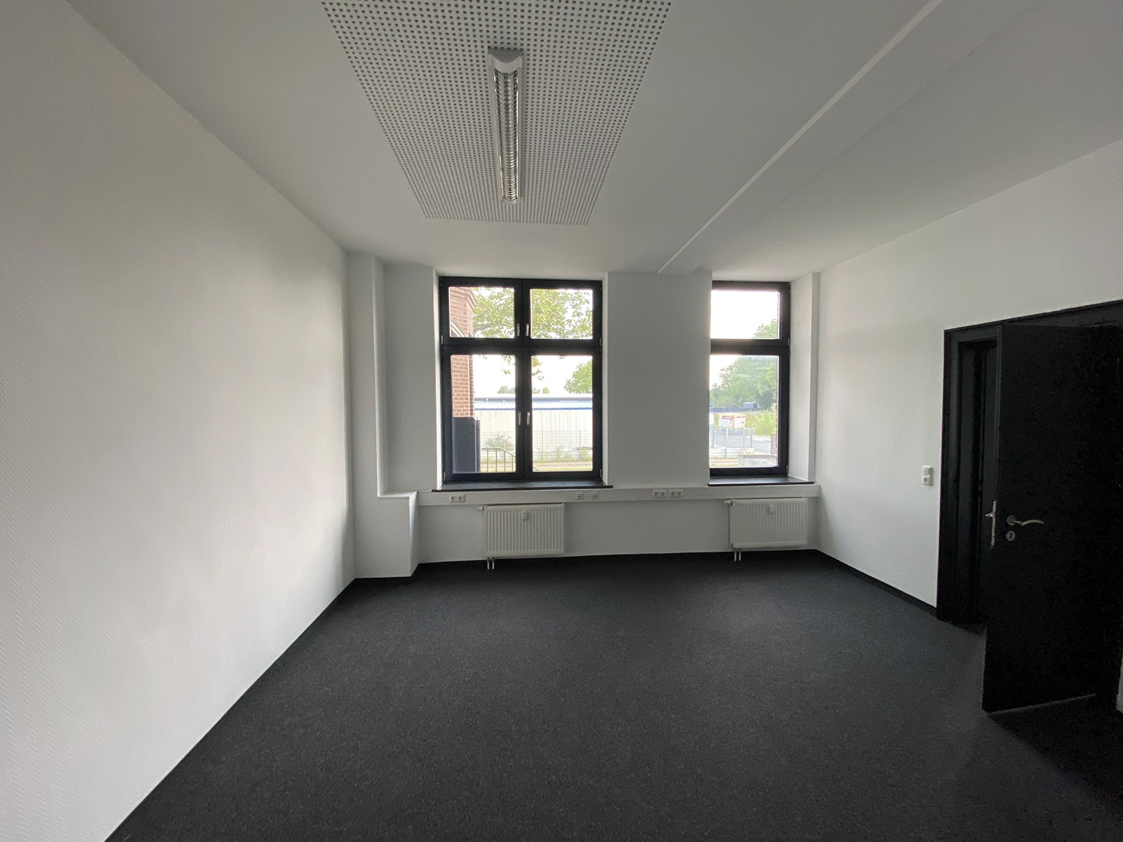 Renovierter Büroraum EG1 mit dunklem Teppichboden und großen Fenstern