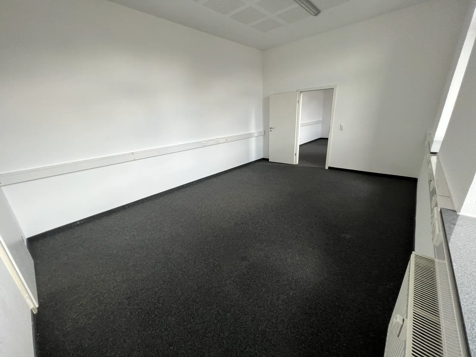 Büroraum mit dunklem Teppichboden und Tageslicht